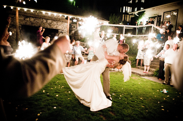 Groom dipping and kissing bride at reception as guests hold sparklers - photo by Portland wedding photographer Barbie Hull 
